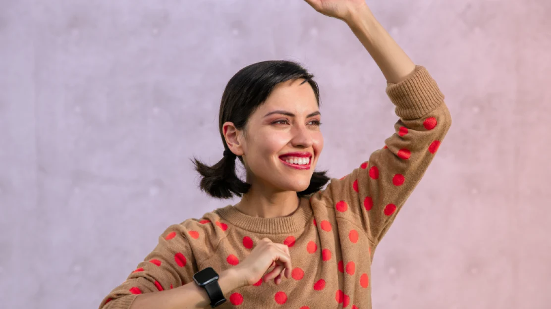 April Proano smiling and waving in a polka-dot sweater